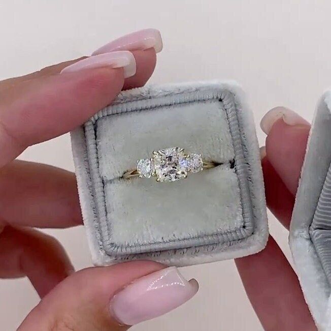 a woman's hand holding an engagement ring in a velvet box with the diamond set on it