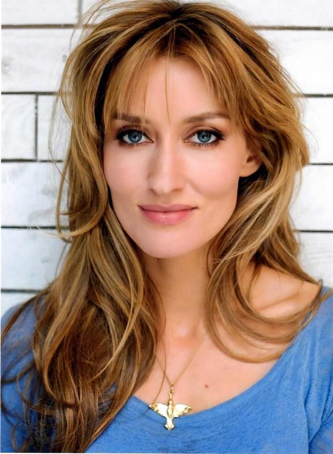 a close up of a person with long hair wearing a blue shirt and gold necklace