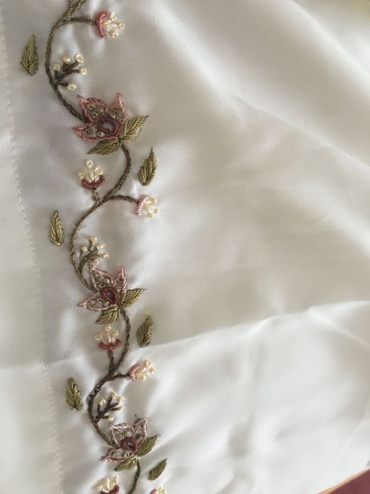 an embroidered piece of cloth with flowers and leaves on it's side, laying on top of a bed