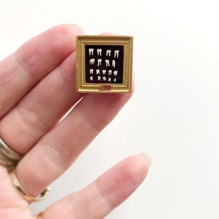 a person is holding a small gold and black square brooch with hebrew symbols on it