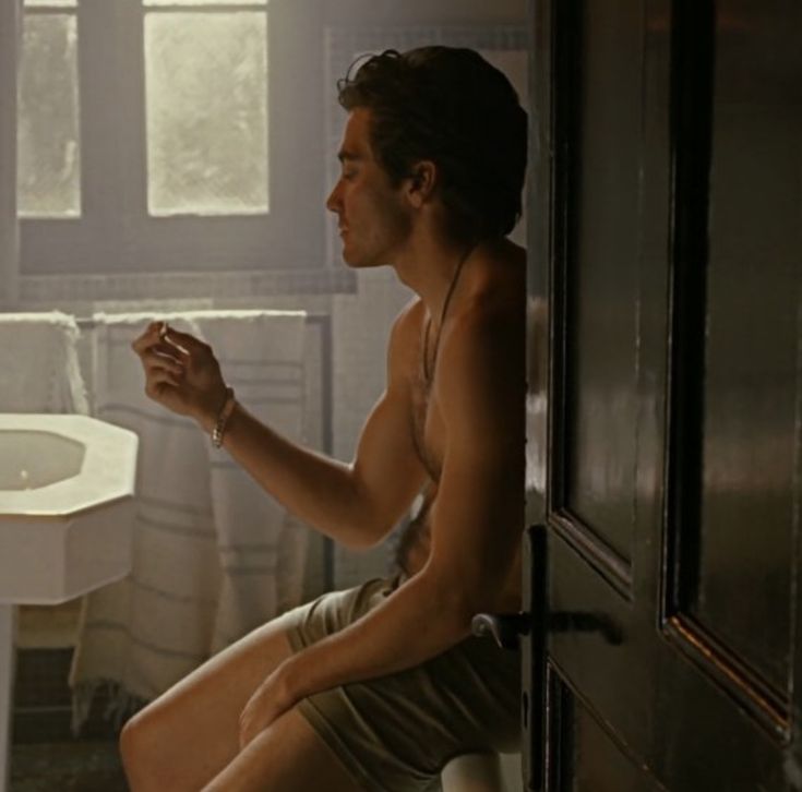 a shirtless man sitting on a toilet next to a sink