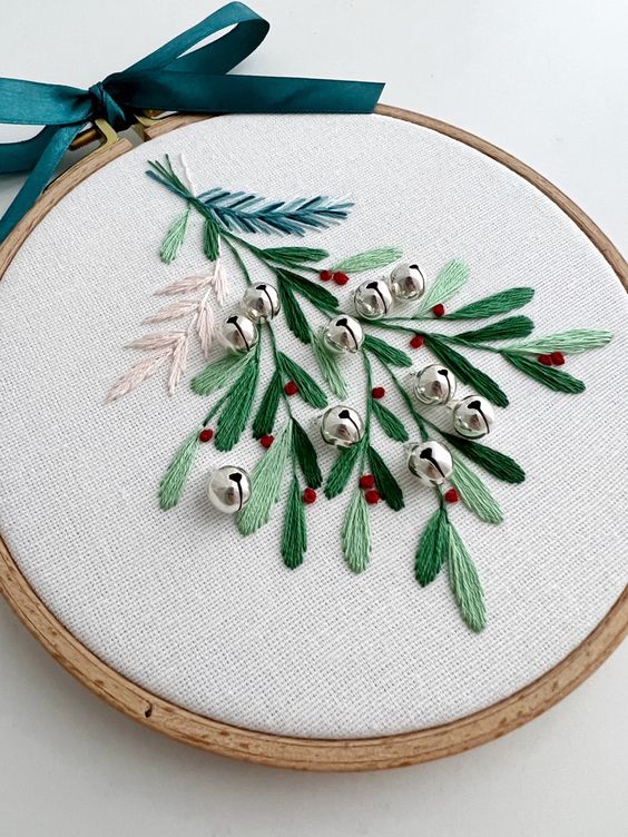 an embroidered christmas ornament with bells and holly leaves on white fabric in a wooden hoop