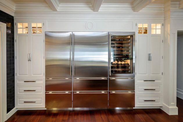 a stainless steel refrigerator in a kitchen with wood floors and white cabinets on either side