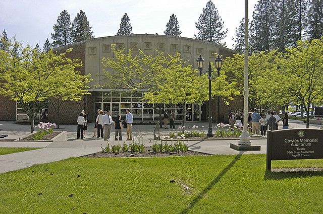 several people are standing in front of a building with many trees on the side walk