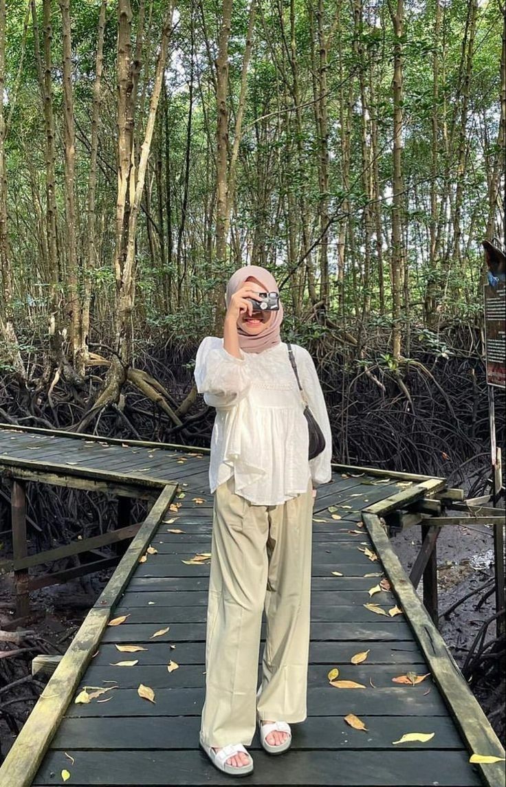 a woman standing on a wooden bridge in the woods taking a photo with her cell phone