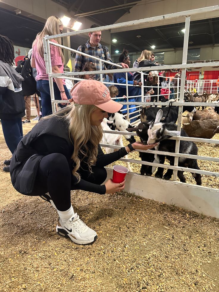 a woman petting two baby goats in a pen at a livestock show with other people looking on