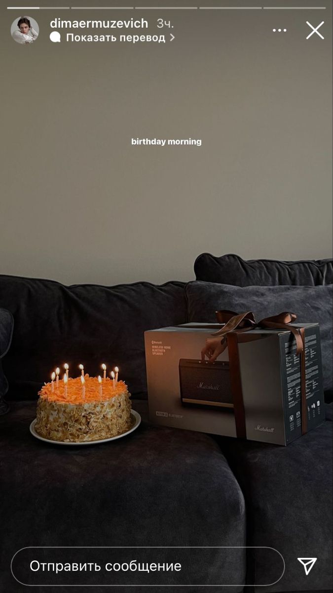 a birthday cake sitting on top of a couch next to a box with lit candles