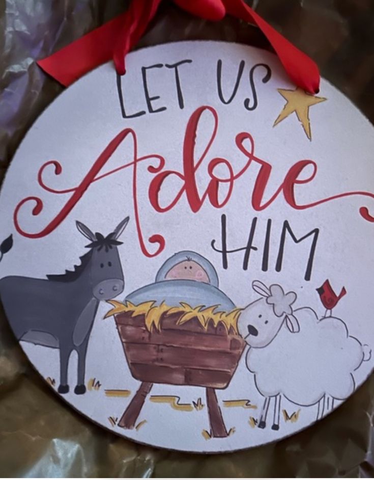 a christmas ornament that says let us adore him with two animals and a baby in a manger