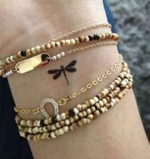 a woman's arm with three bracelets on it and a dragonfly tattoo