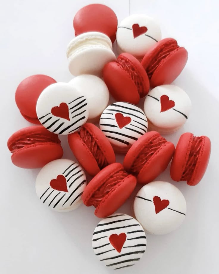 red and white macaroons with hearts painted on them are arranged in a pile