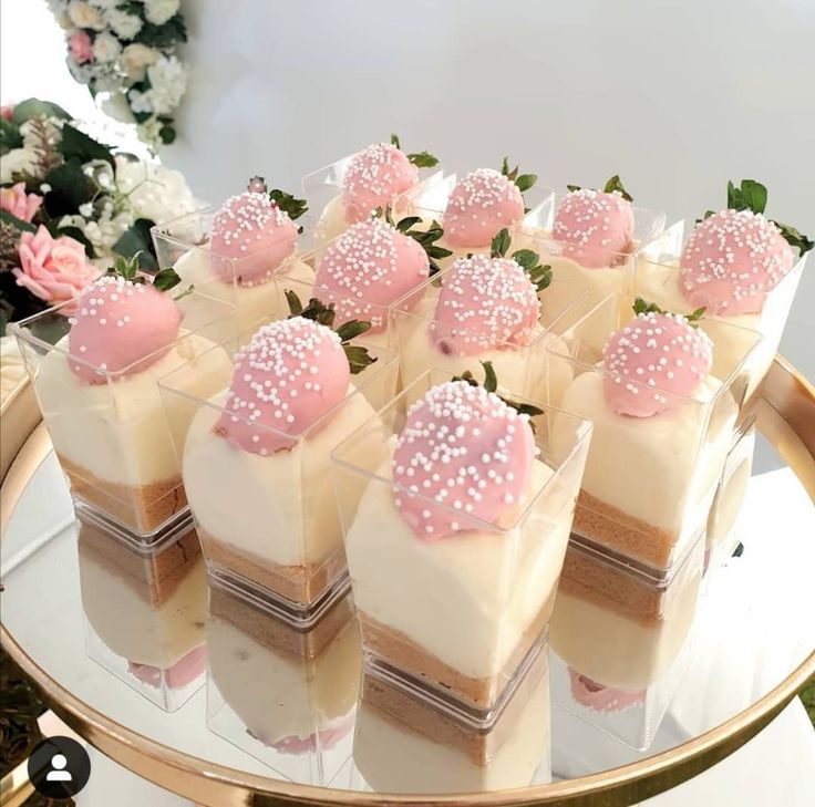 there are many small desserts on the glass platter with pink frosting and sprinkles