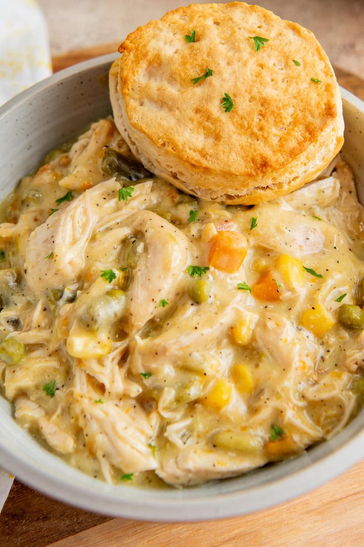 a white bowl filled with chicken pot pie and corn chowdery next to a biscuit