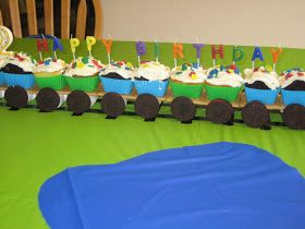 birthday cupcakes are arranged on top of train tracks in front of a green tablecloth