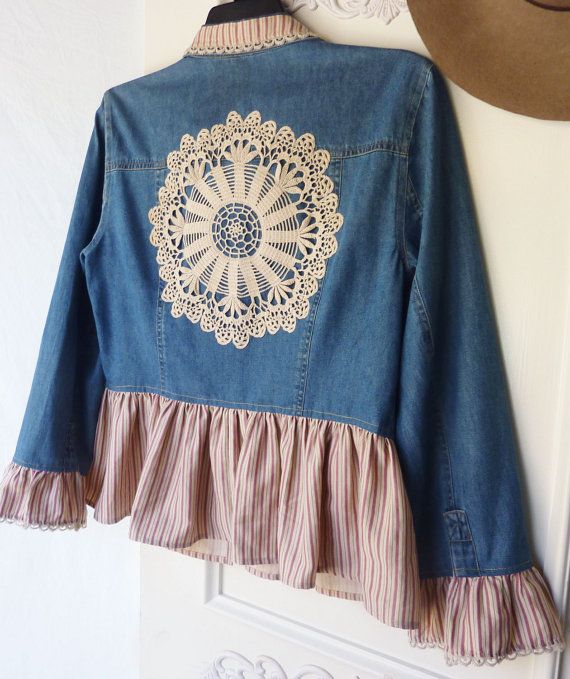 a blue jean jacket with white lace and ruffles hanging on a wall next to a hat