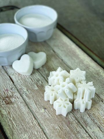 some sugar cubes are on a wooden table next to two bowls and spoons