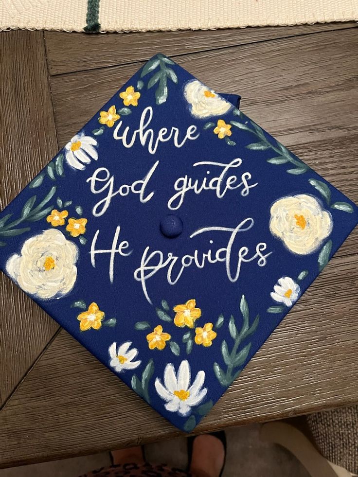 a blue graduation cap with white and yellow flowers on it that says, where god guides he provides