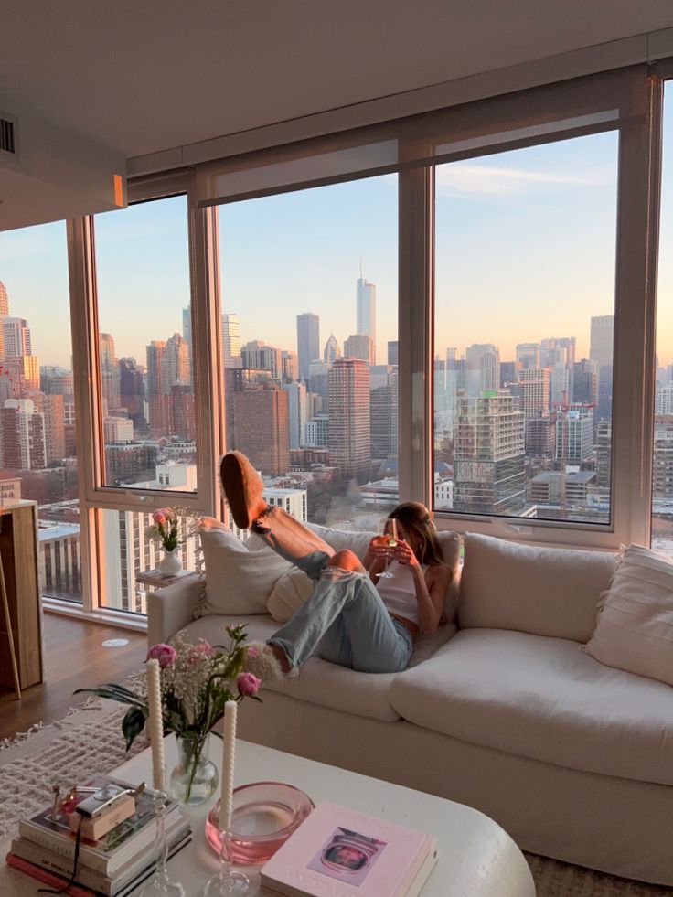 two people sitting on a couch in front of large windows with the city skyline outside