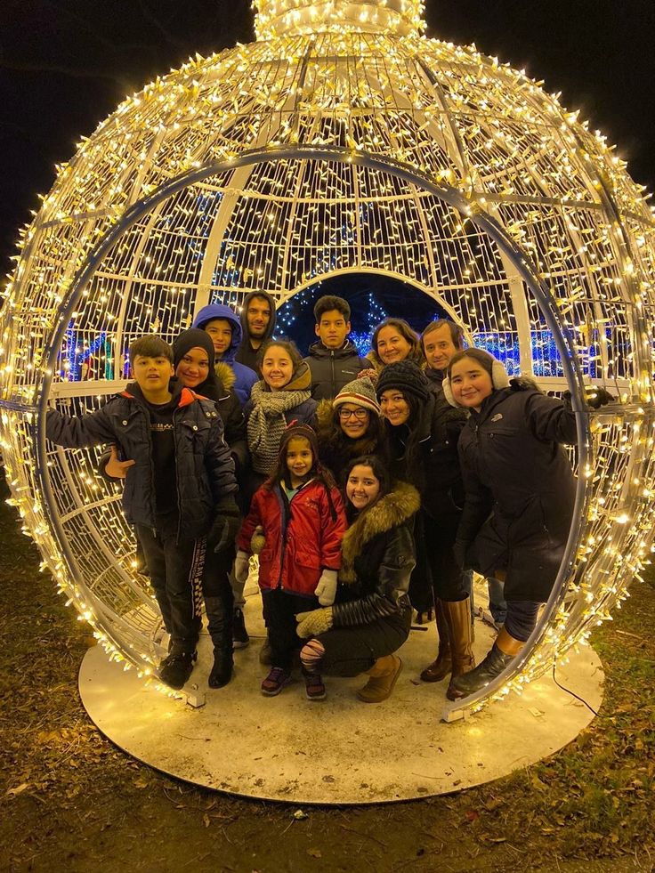 a group of people standing in front of a christmas light ball with lights on it