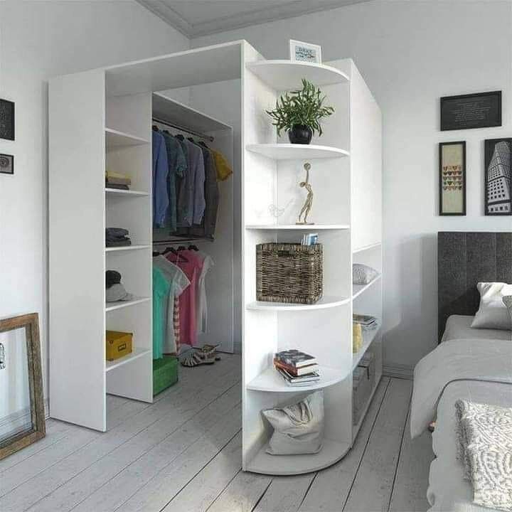 a bedroom with white walls and flooring has an open closet in the corner that is next to a bed