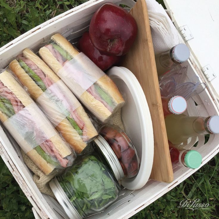 the picnic basket is filled with sandwiches, apples, and jars of pickled fruit