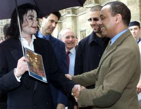 two men shaking hands with one another while other people stand in the background holding umbrellas