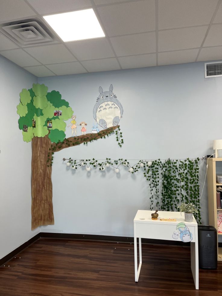 an office with a tree and totoro wall decal on the wall next to a white desk