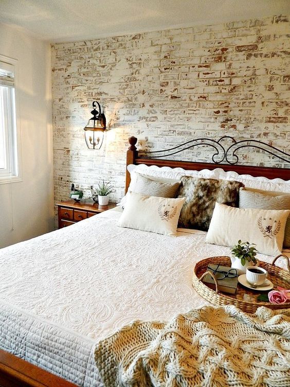 a bed with white sheets and pillows in a bedroom next to a brick wall that has an iron headboard