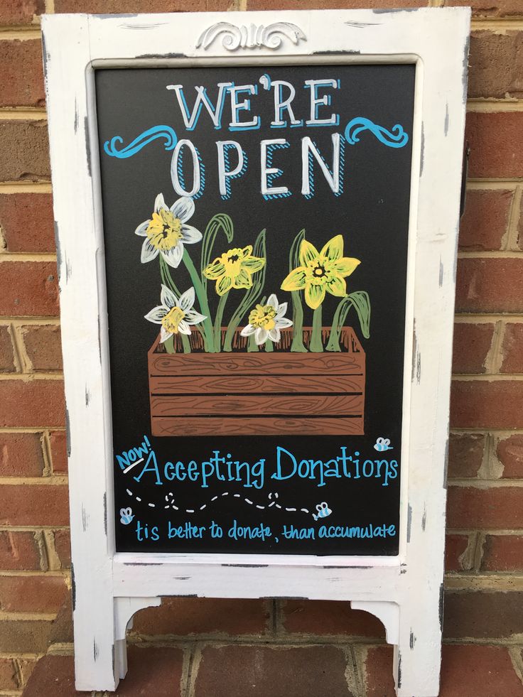 a chalkboard sign with daffodils painted on it that says, we're open