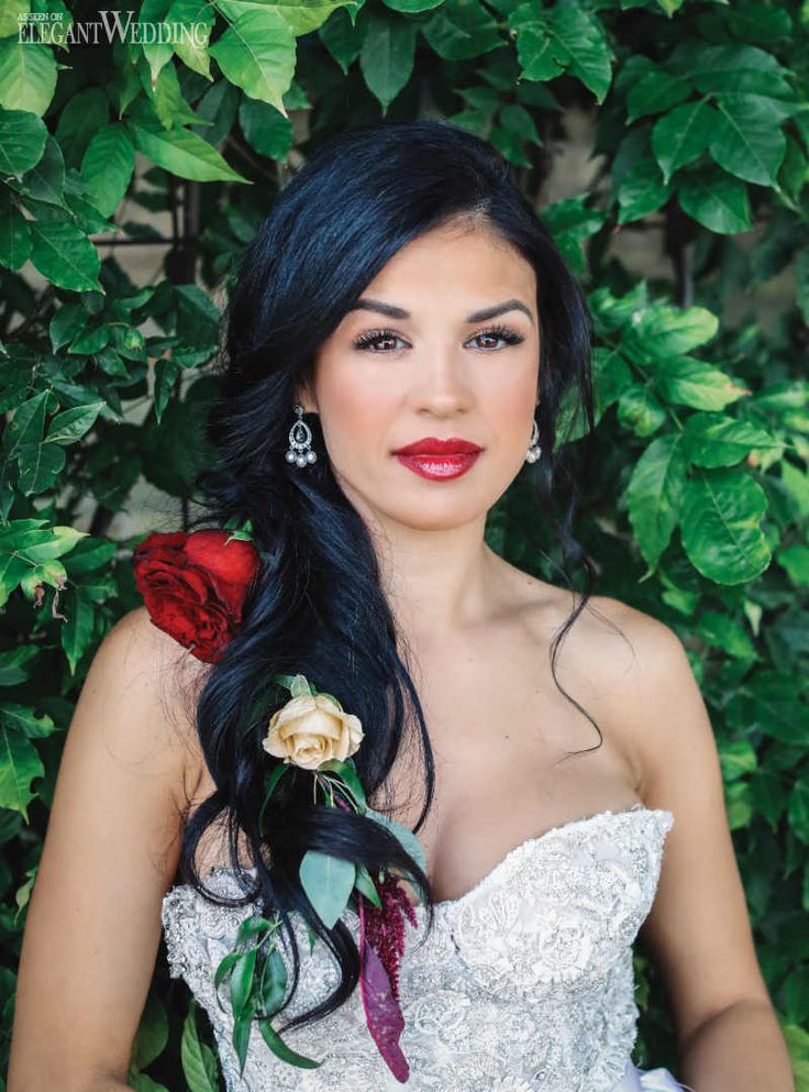 a woman with long black hair wearing a white dress and red roses in her hair