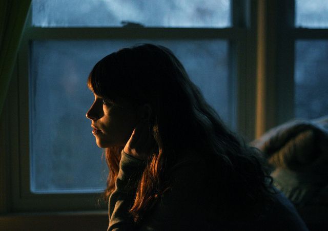 a woman sitting in front of a window talking on a cell phone while looking out the window