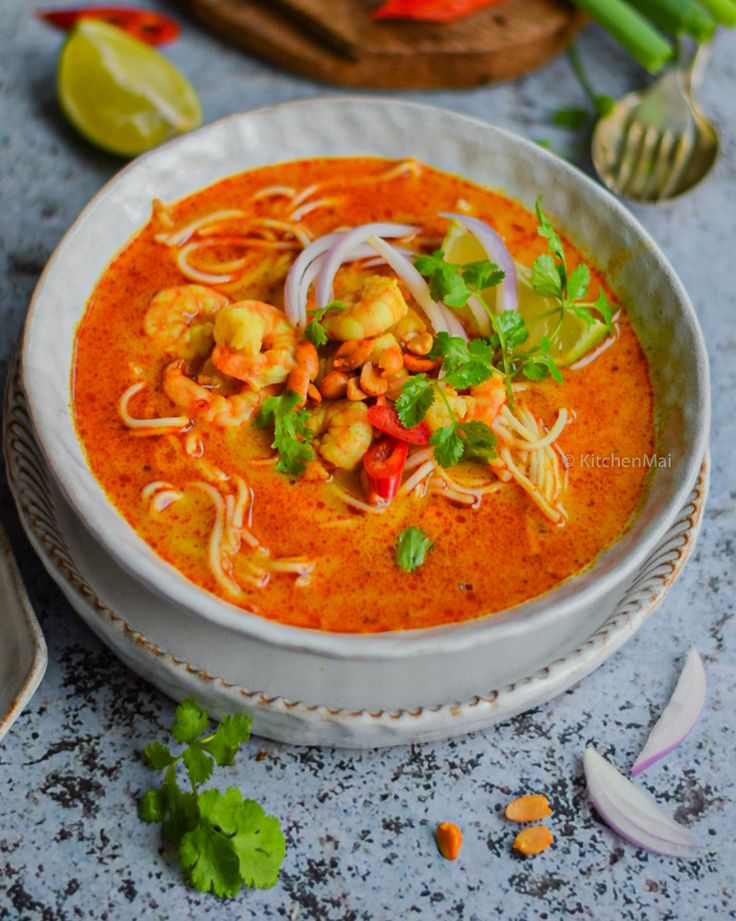 a white bowl filled with shrimp and noodle soup on top of a blue counter