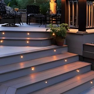 some lights are lit up on the steps to an outdoor patio area with chairs and tables