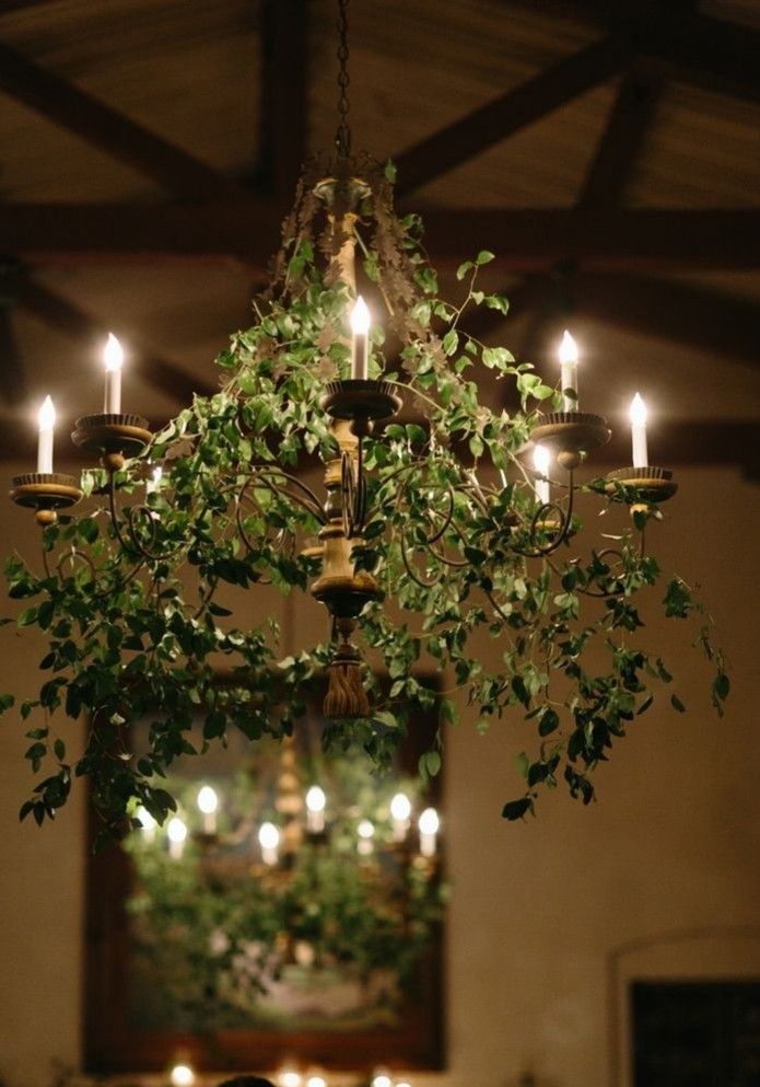 a chandelier with candles hanging from it's ceiling and greenery in the middle