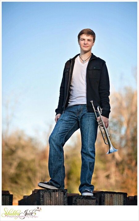 a young man holding a trumpet and standing on top of some blocks with trees in the background