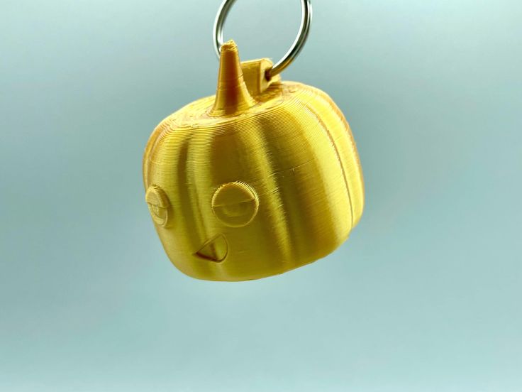 a yellow plastic pumpkin shaped keychain hanging from a metal hook on a blue background