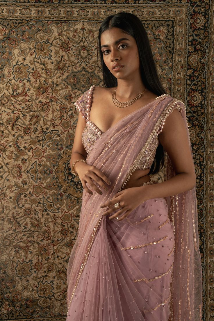 This dusty pink saree is a vision of elegance, crafted from shimmering tissue fabric that glimmers with every movement. Paired with a raw silk blouse, the ensemble exudes sophistication and charm. The intricately hand-embroidered blouse adds a touch of glamour, making it perfect for a cocktail or reception, whether for the bride or her bridesmaids. With its timeless allure and delicate detailing, this saree is sure to captivate attention and leave a lasting impression on any special occasion.Fro Celebrity Lehenga Outfits, Pink Saree With Pink Blouse, Blouse For Wedding For Women, Cocktail Saree Blouse, Dusky Pink Saree, Blouse Designs On Silk Saree, Pretty Sarees Beautiful, Blouse Design Aesthetic, Bridesmaid Saree Ideas