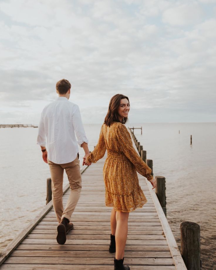 a man and woman walking on a pier holding hands