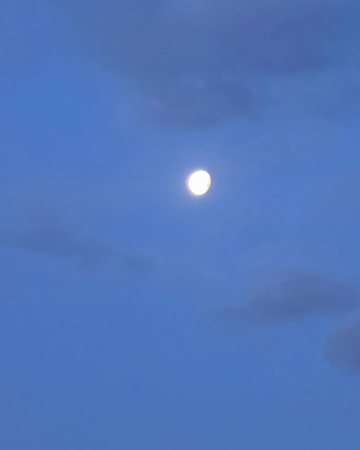 an airplane flying in the sky at night with the moon behind it and some clouds