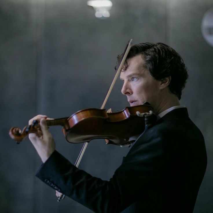 a man holding a violin in his right hand and wearing a suit on the other