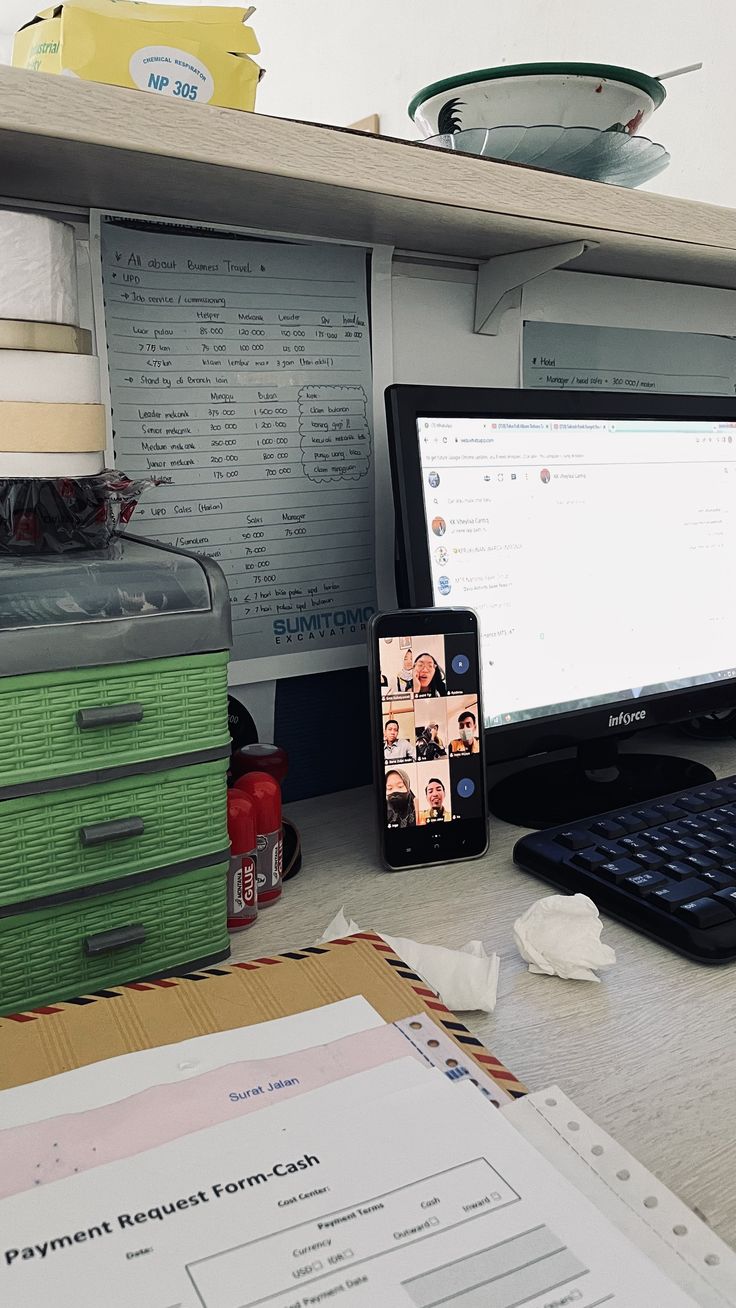 a computer monitor, keyboard and cell phone on a cluttered desk with papers in front of it