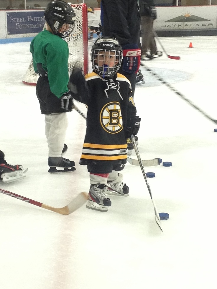 two young hockey players are standing on the ice with their sticks in hand while an adult watches