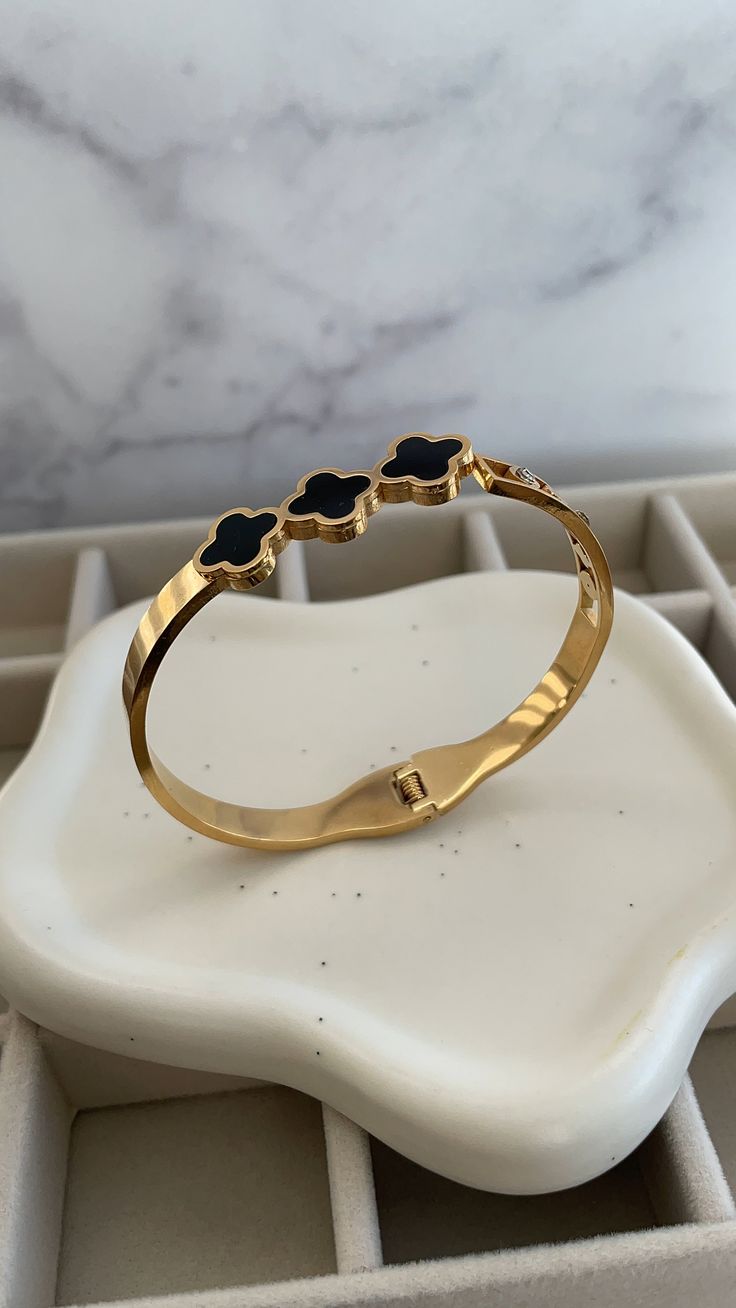 ✨Elevate your elegance with this exquisite gold bangle, a masterpiece that combines sophistication and sensuality. ✨Crafted with sleek gold and adorned with delicate black enamel clover motifs, this bracelet adds a touch of luxury to any ensemble. ✨The glimmering gold catches the light with every movement, while the bold clovers symbolize grace and allure. ✨A subtle diamond accent adds a hint of sparkle, making this piece the perfect companion for both day and night. Slip it on, and feel the con Timeless Black Bangle Jewelry, Elegant Black Enamel Bangle Bracelet, Elegant Black Enamel Bracelets As Gift, Elegant Black Enamel Bangle For Gift, Elegant Black Enamel Bangle Gift, Luxury Gold Bangle With Black Enamel, Elegant Black Bangle Gold Bracelet, Black Gold-plated Bracelets, Elegant Black Bangle Bracelet