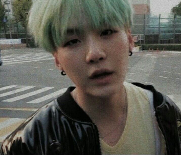 a young man with green hair and piercings on his ears standing in the street