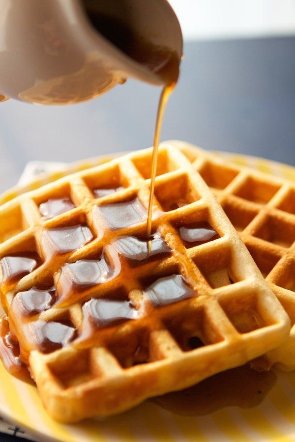 a person pouring syrup on top of a waffles that are sitting on a yellow and white plate