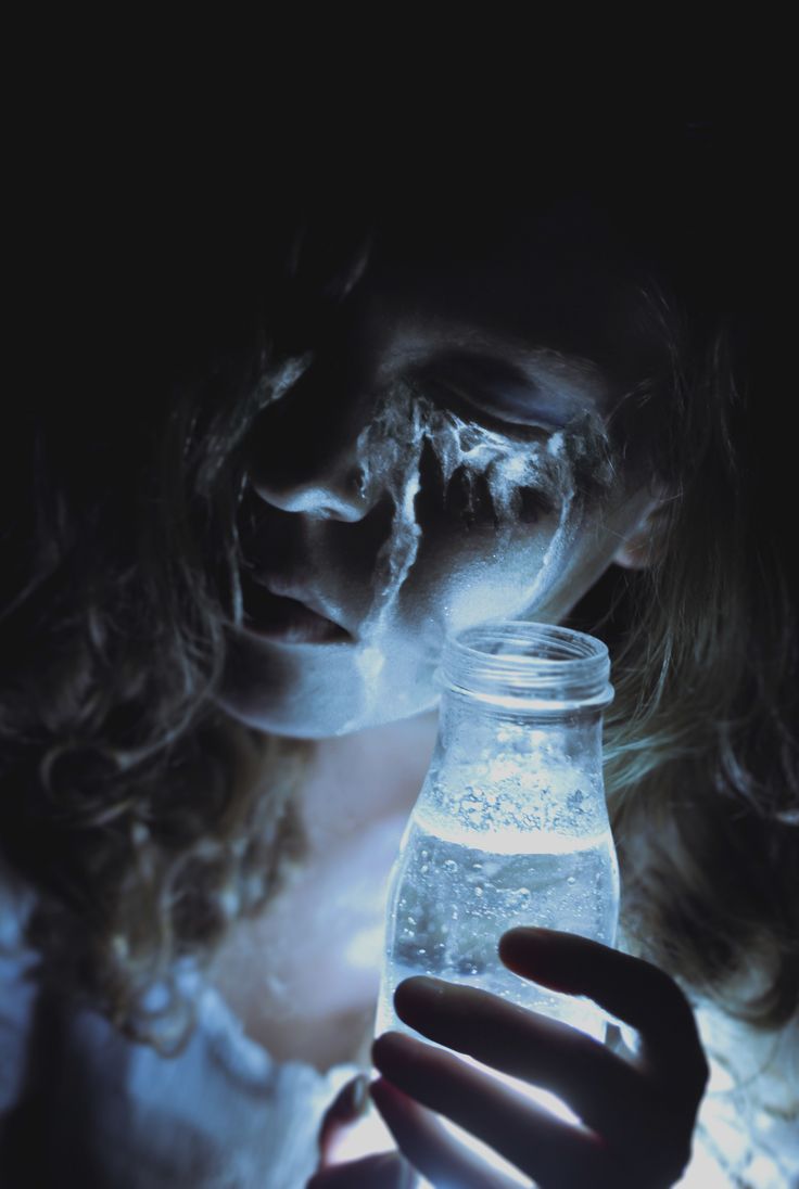 a woman holding a glass jar with water in it's mouth and light coming from behind her