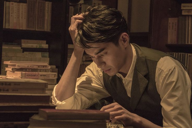 a man sitting at a desk in front of a stack of books with his hand on his head