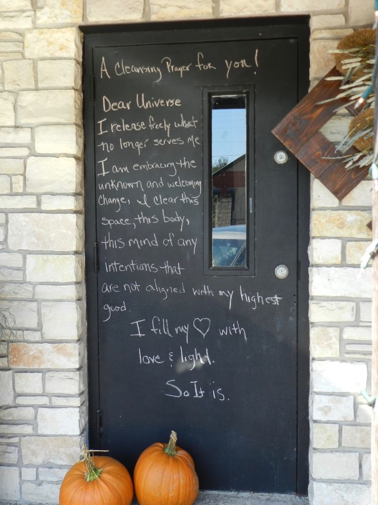 two pumpkins sitting in front of a black door with writing on the outside wall