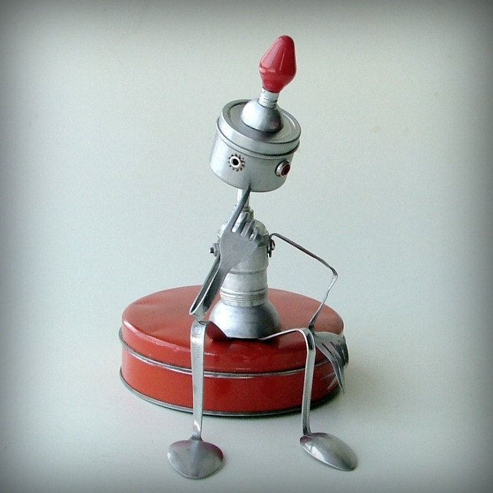 a toy robot sitting on top of a red box with two spoons in it