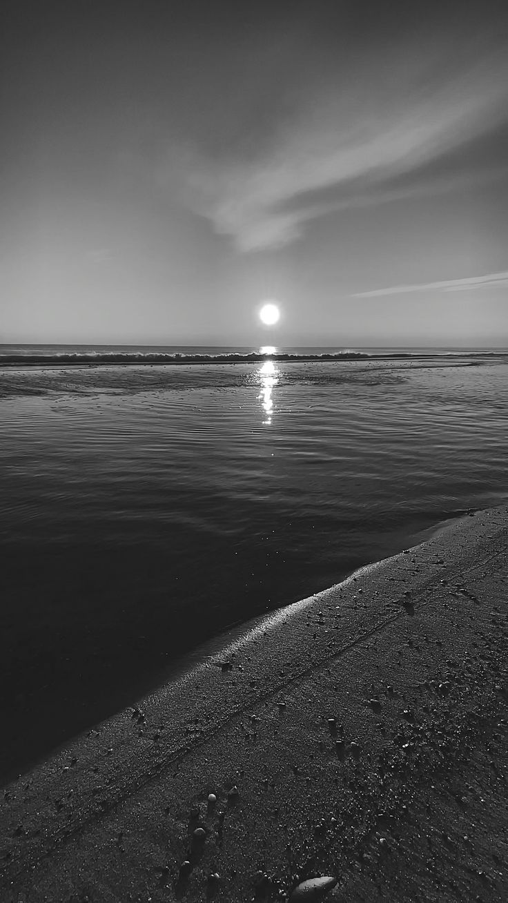 a black and white photo of the sun setting over water