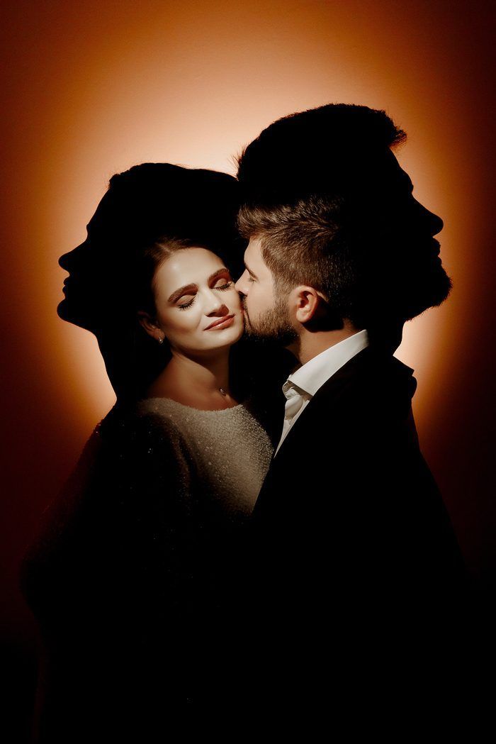 a man and woman are posing for a photo in front of a dark background with the light coming through them